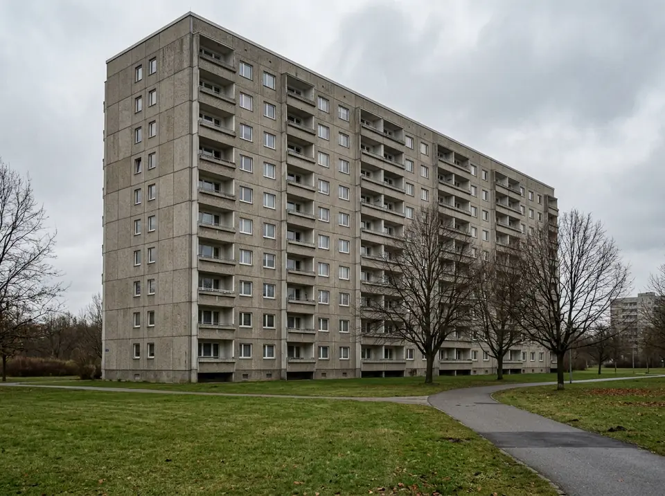 Többemeletes panelház homlokzata erkélysorokkal, előtte füves terület
